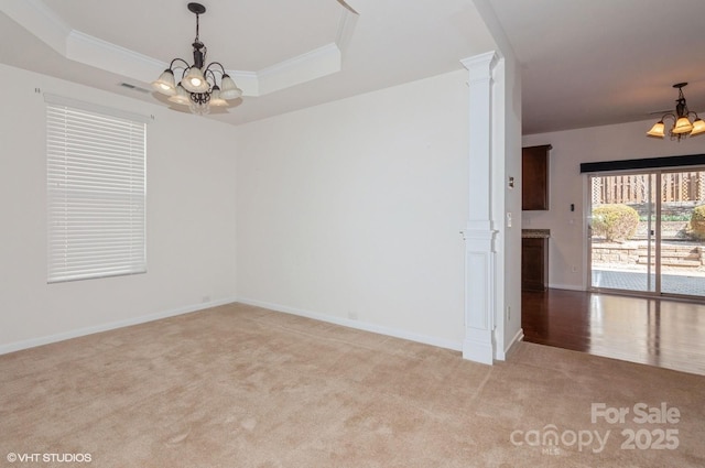 spare room featuring a chandelier, light carpet, a raised ceiling, and decorative columns