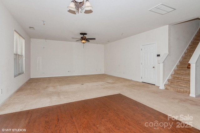 carpeted empty room with ceiling fan, stairway, and visible vents