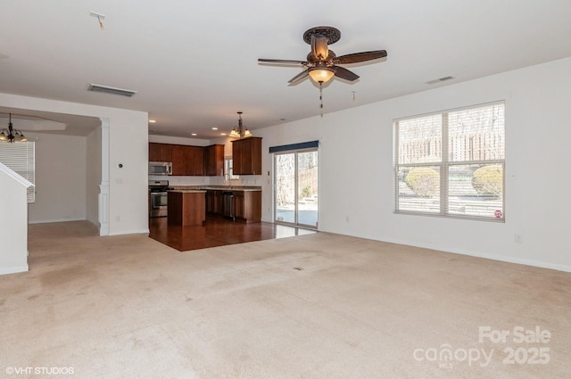 unfurnished living room with ceiling fan with notable chandelier, dark colored carpet, visible vents, and recessed lighting