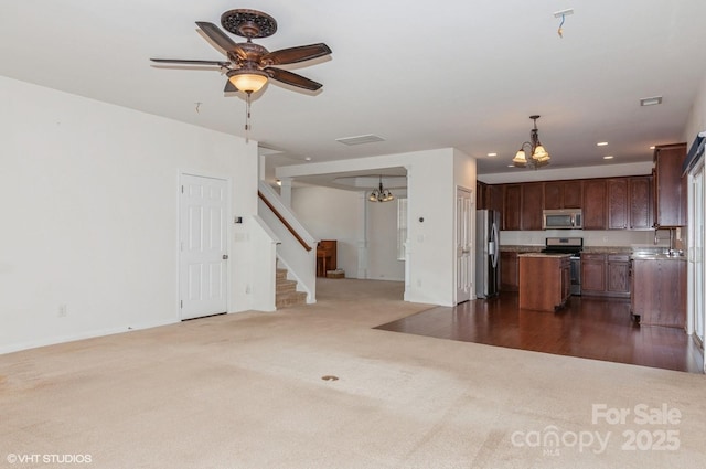 unfurnished living room featuring stairway, ceiling fan with notable chandelier, dark colored carpet, a sink, and recessed lighting