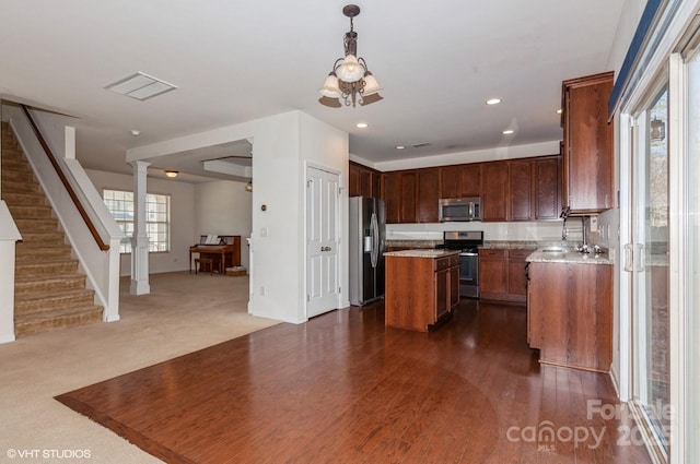 kitchen featuring a center island, decorative columns, stainless steel appliances, hanging light fixtures, and open floor plan