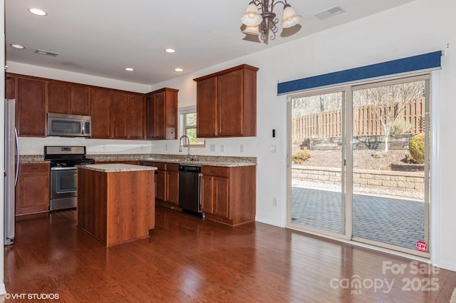 kitchen featuring dark wood-style floors, a center island, visible vents, hanging light fixtures, and appliances with stainless steel finishes