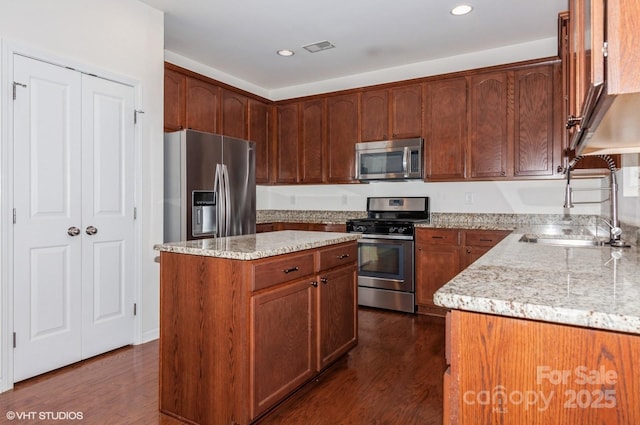 kitchen featuring brown cabinetry, a kitchen island, light stone counters, dark wood-style flooring, and stainless steel appliances