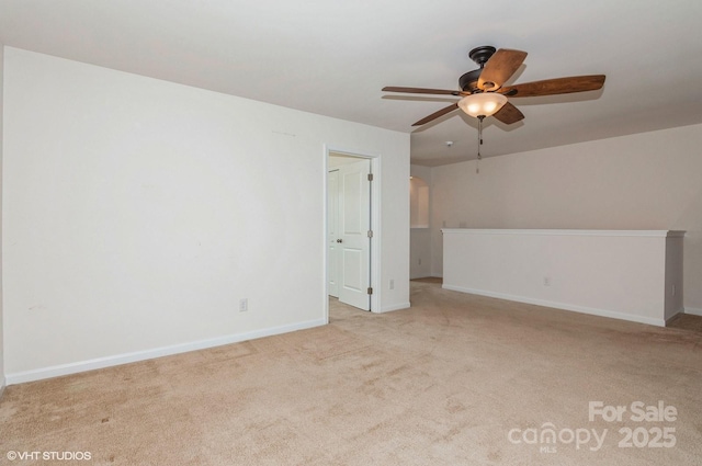 interior space featuring baseboards, a ceiling fan, and light colored carpet