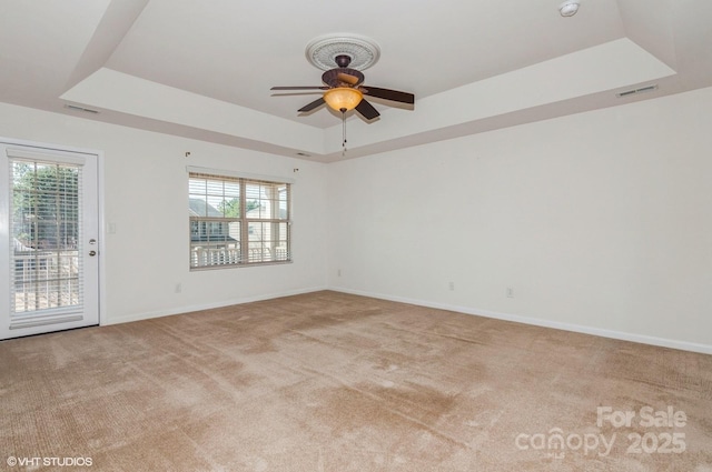 empty room featuring visible vents, baseboards, a raised ceiling, light colored carpet, and ceiling fan