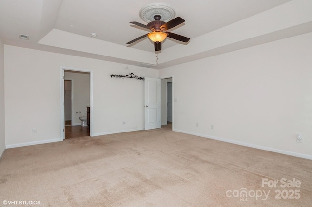 unfurnished bedroom featuring baseboards, visible vents, a tray ceiling, and light colored carpet