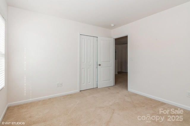 unfurnished bedroom with a closet, light colored carpet, and baseboards