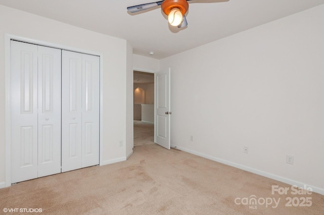 unfurnished bedroom with a closet, light colored carpet, ceiling fan, and baseboards