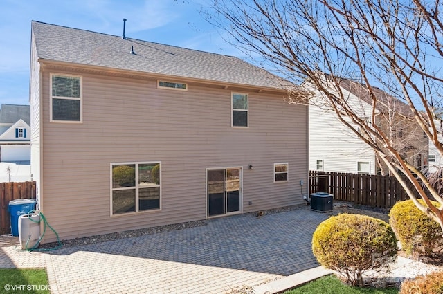 rear view of property with a shingled roof, fence, central AC unit, and a patio