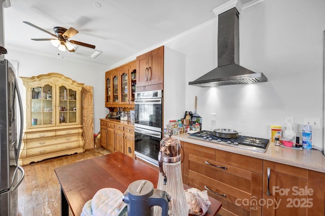 kitchen with crown molding, ceiling fan, appliances with stainless steel finishes, light hardwood / wood-style floors, and wall chimney exhaust hood