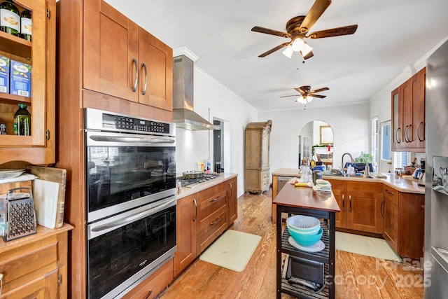 kitchen featuring range hood, sink, light hardwood / wood-style floors, stainless steel appliances, and crown molding