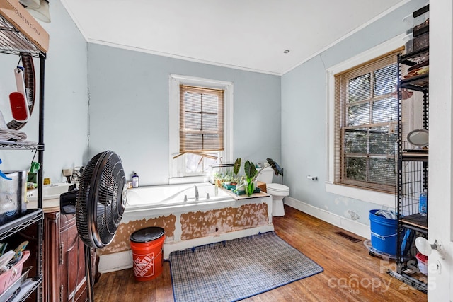 bathroom with a tub to relax in, crown molding, wood-type flooring, and toilet