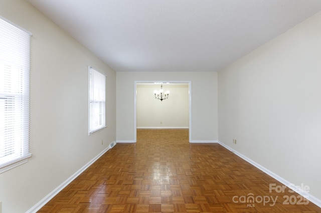 unfurnished room with dark parquet flooring, a healthy amount of sunlight, and a chandelier