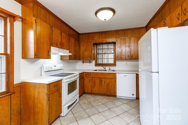 kitchen featuring sink, a textured ceiling, light tile patterned floors, wooden walls, and white appliances