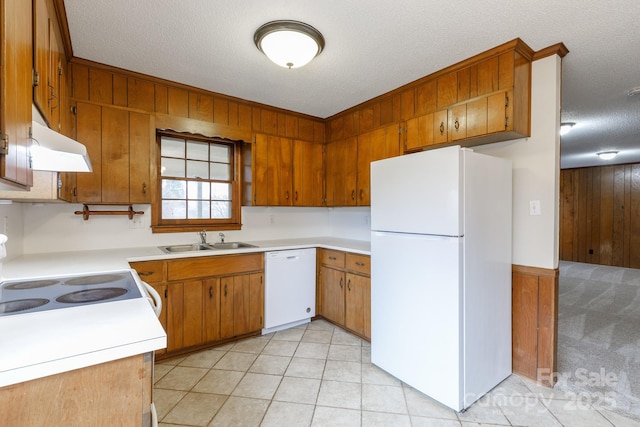 kitchen featuring sink, wood walls, a textured ceiling, light tile patterned floors, and white appliances