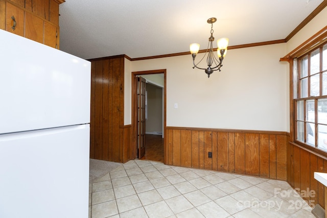 unfurnished dining area with crown molding, light tile patterned flooring, a chandelier, and wood walls