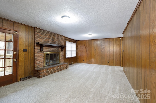 unfurnished living room featuring carpet flooring, a textured ceiling, a fireplace, and wood walls