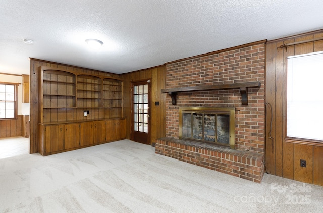 unfurnished living room with light colored carpet, a fireplace, a textured ceiling, and wood walls