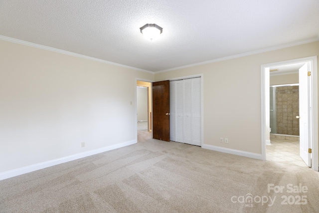 unfurnished bedroom with ensuite bath, ornamental molding, a textured ceiling, light colored carpet, and a closet