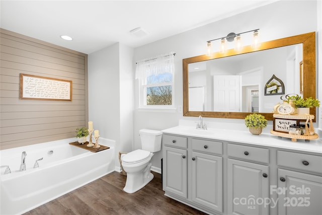 bathroom featuring a tub to relax in, wood walls, toilet, vanity, and hardwood / wood-style floors