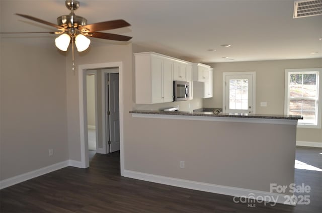 kitchen with dark hardwood / wood-style floors, kitchen peninsula, ceiling fan, dark stone counters, and white cabinets