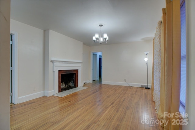 unfurnished living room with an inviting chandelier, a fireplace, and light hardwood / wood-style floors