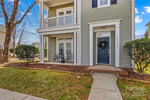 view of exterior entry featuring a balcony, a porch, and a lawn