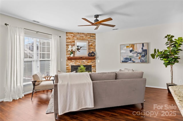 living room featuring baseboards, visible vents, dark wood-style floors, ceiling fan, and a stone fireplace