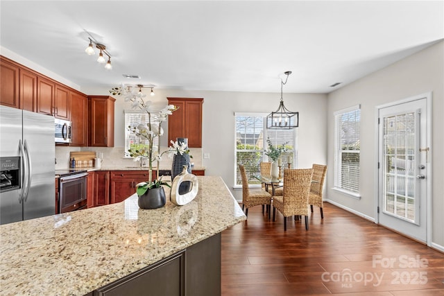 kitchen with hanging light fixtures, appliances with stainless steel finishes, light stone countertops, dark wood-style floors, and an inviting chandelier