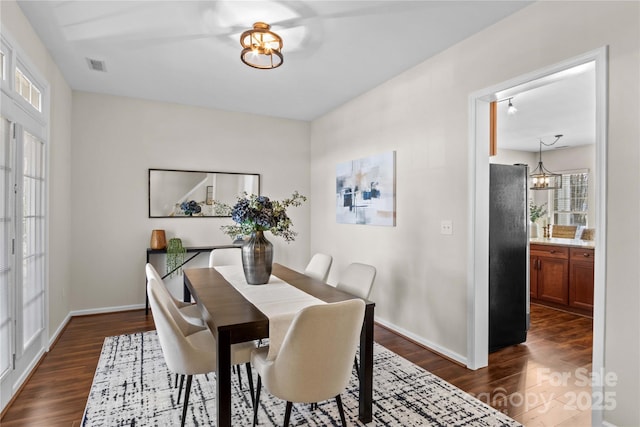 dining space with a chandelier, dark wood-type flooring, visible vents, and baseboards