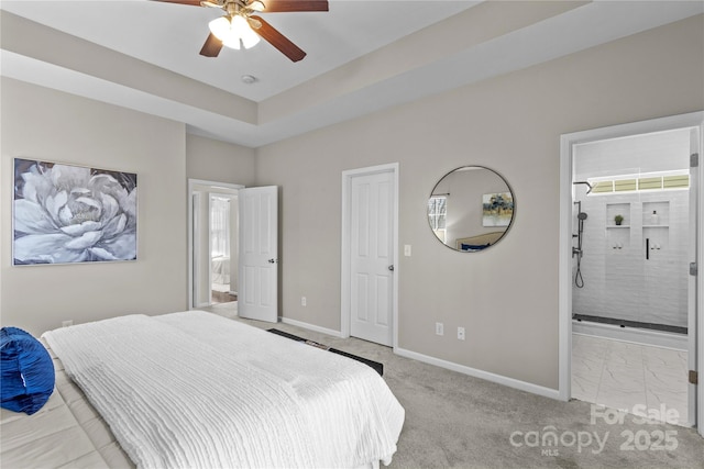 bedroom featuring a raised ceiling, ensuite bath, light colored carpet, and baseboards