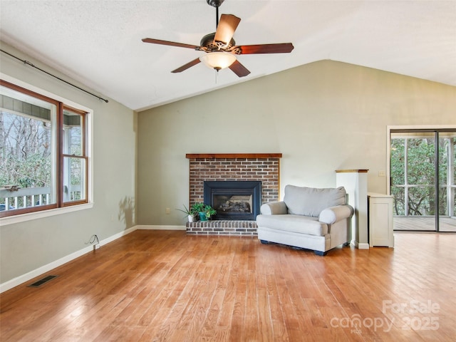 living room featuring lofted ceiling, a fireplace, light hardwood / wood-style floors, and ceiling fan