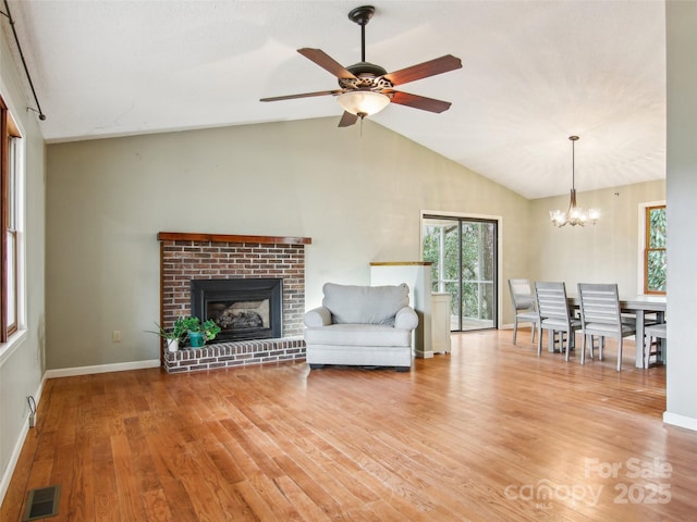 unfurnished living room with lofted ceiling, a brick fireplace, ceiling fan with notable chandelier, and light hardwood / wood-style flooring