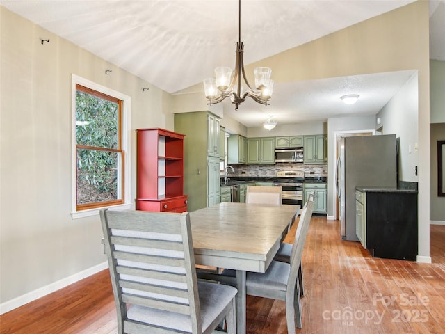 dining room featuring sink, vaulted ceiling, a textured ceiling, light hardwood / wood-style flooring, and a notable chandelier