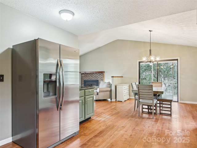 kitchen with vaulted ceiling, decorative light fixtures, green cabinetry, stainless steel refrigerator with ice dispenser, and light hardwood / wood-style flooring