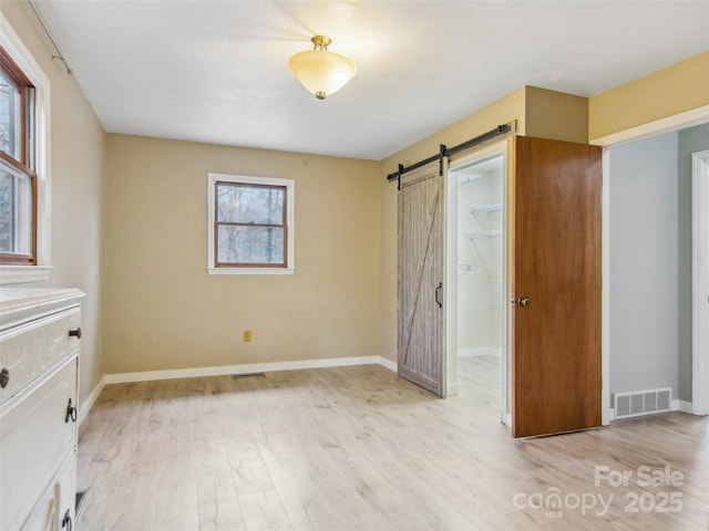 unfurnished bedroom featuring a spacious closet, a barn door, a closet, and light wood-type flooring