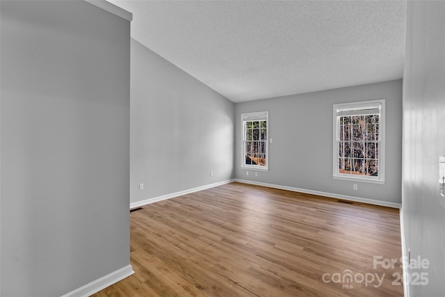 empty room featuring visible vents, baseboards, a textured ceiling, and wood finished floors