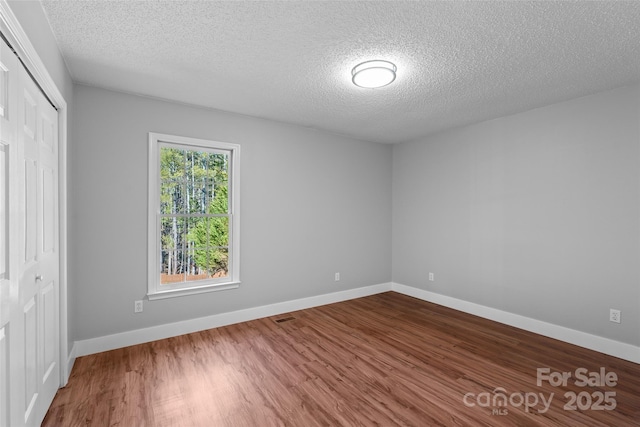 unfurnished bedroom featuring a closet, baseboards, a textured ceiling, and wood finished floors