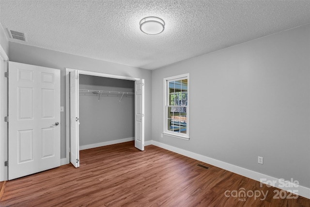 unfurnished bedroom with wood finished floors, visible vents, a closet, and baseboards