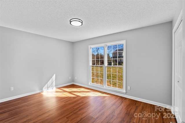 spare room featuring wood finished floors, baseboards, and a textured ceiling