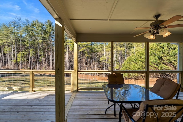 wooden terrace featuring a wooded view, outdoor dining area, and ceiling fan