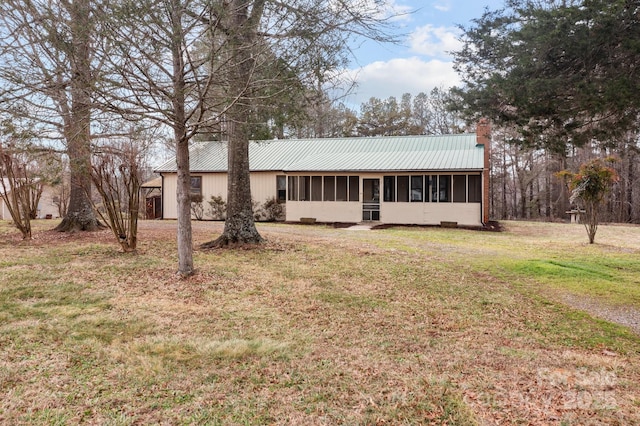 view of front of home featuring a sunroom, a chimney, metal roof, and a front yard
