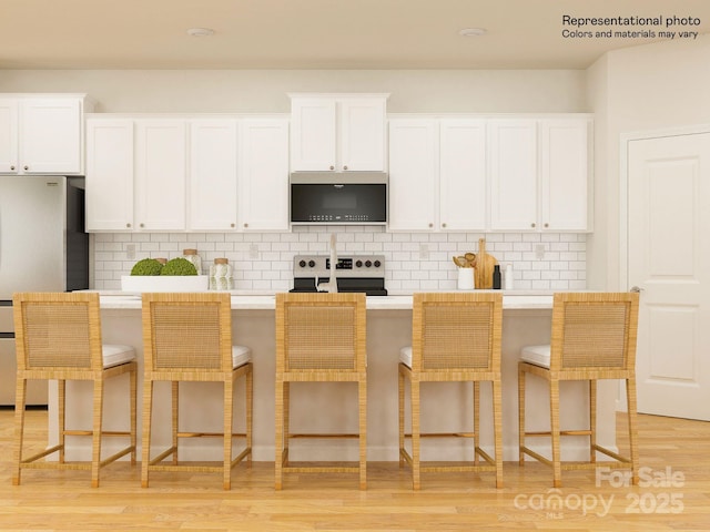 kitchen featuring a center island with sink, light wood-style flooring, freestanding refrigerator, range with electric stovetop, and white cabinetry