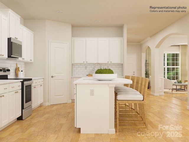 kitchen with electric range, a sink, arched walkways, a breakfast bar area, and white cabinets