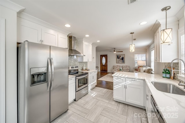 kitchen with a sink, open floor plan, appliances with stainless steel finishes, wall chimney range hood, and ornamental molding