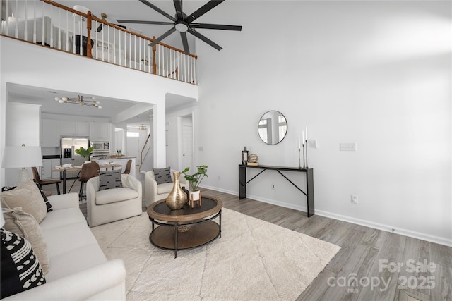 living room with ceiling fan, a high ceiling, and light wood-type flooring