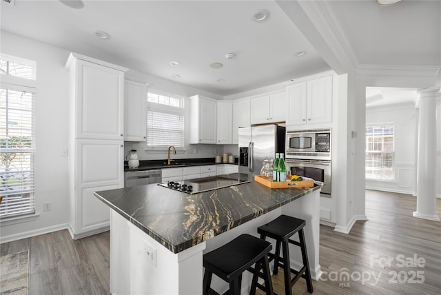 kitchen with white cabinetry, wood-type flooring, a center island, stainless steel appliances, and decorative columns