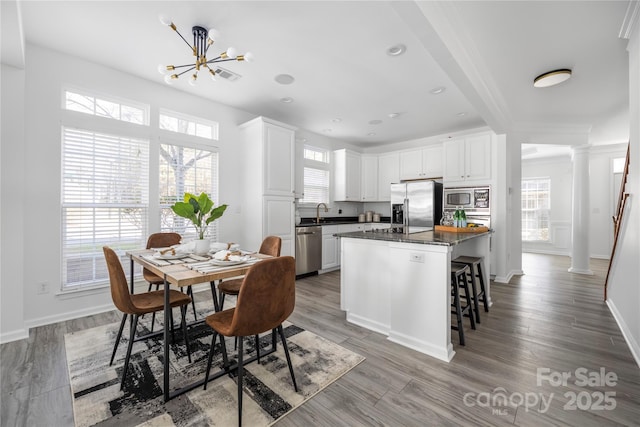 kitchen featuring a kitchen island, appliances with stainless steel finishes, decorative columns, white cabinetry, and dark stone countertops