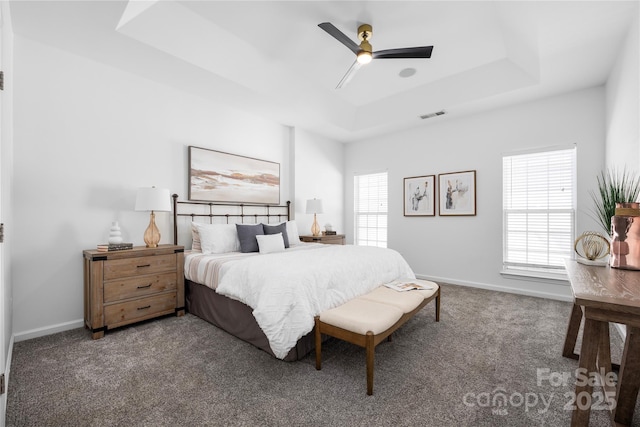 carpeted bedroom featuring multiple windows, a tray ceiling, and ceiling fan