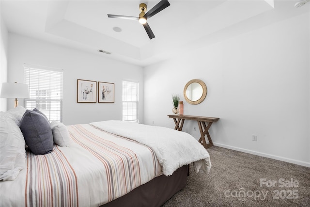 carpeted bedroom featuring ceiling fan, a tray ceiling, and multiple windows